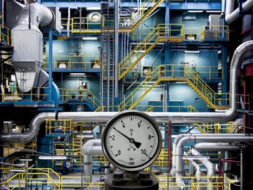 Industrial facility with pipes and a pressure gauge in the foreground.