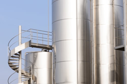 Shiny metal silos with a spiral staircase against a clear blue sky