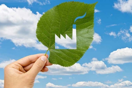leaf with a cut out depiction of a factory with a smokey chimney, being help up to the sky
