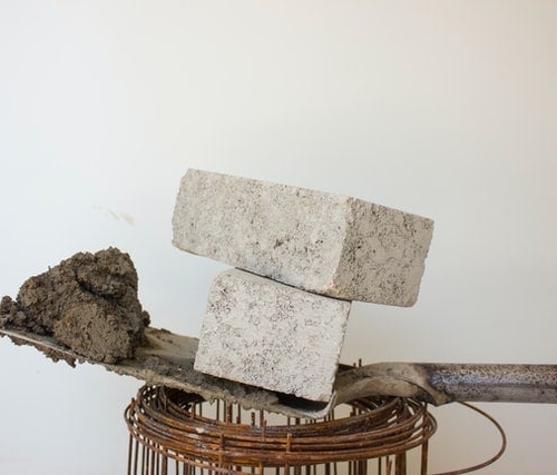 two grey CE-marked cement blocks on top of a shovel, which is on top of rolled-up wires