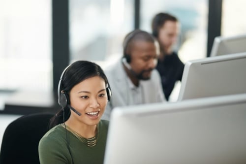 Tre personer med headset sitter i rad framför varsin datorskärm.