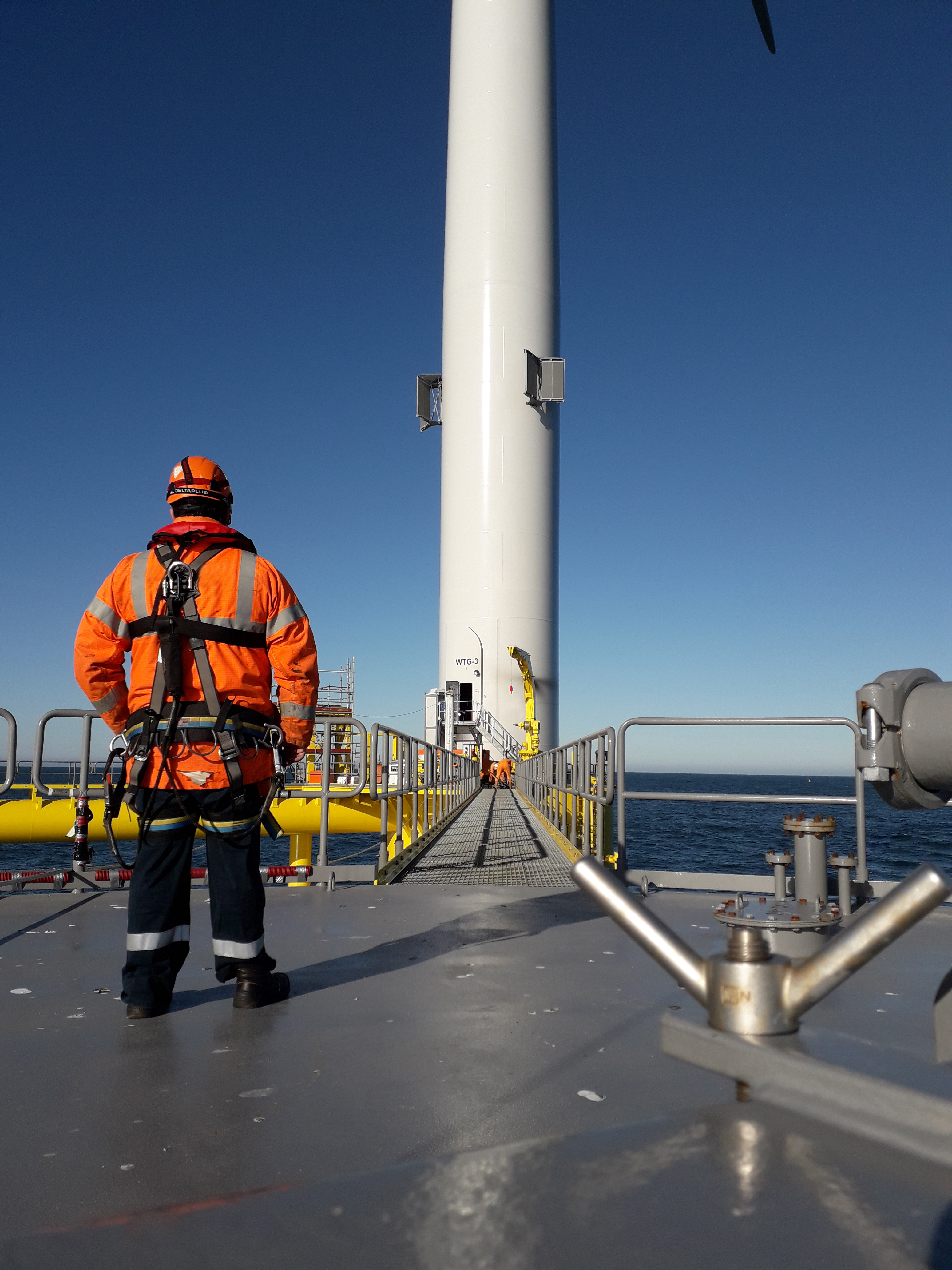 man standing in a platform of a standing windmill, to conduct a non-destructive test on the wind power asset