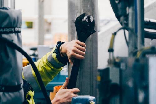 Person använder stor skiftnyckel för att justera maskin.
